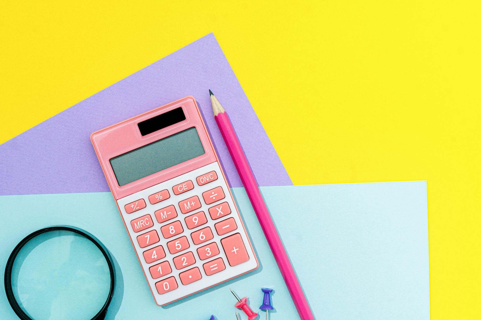 Colorful flat lay of stationery items with a pink calculator on a yellow background.