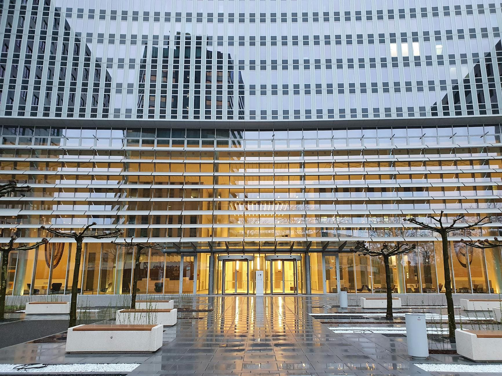Futuristic glass building with reflective facade and entrance illuminated at twilight.