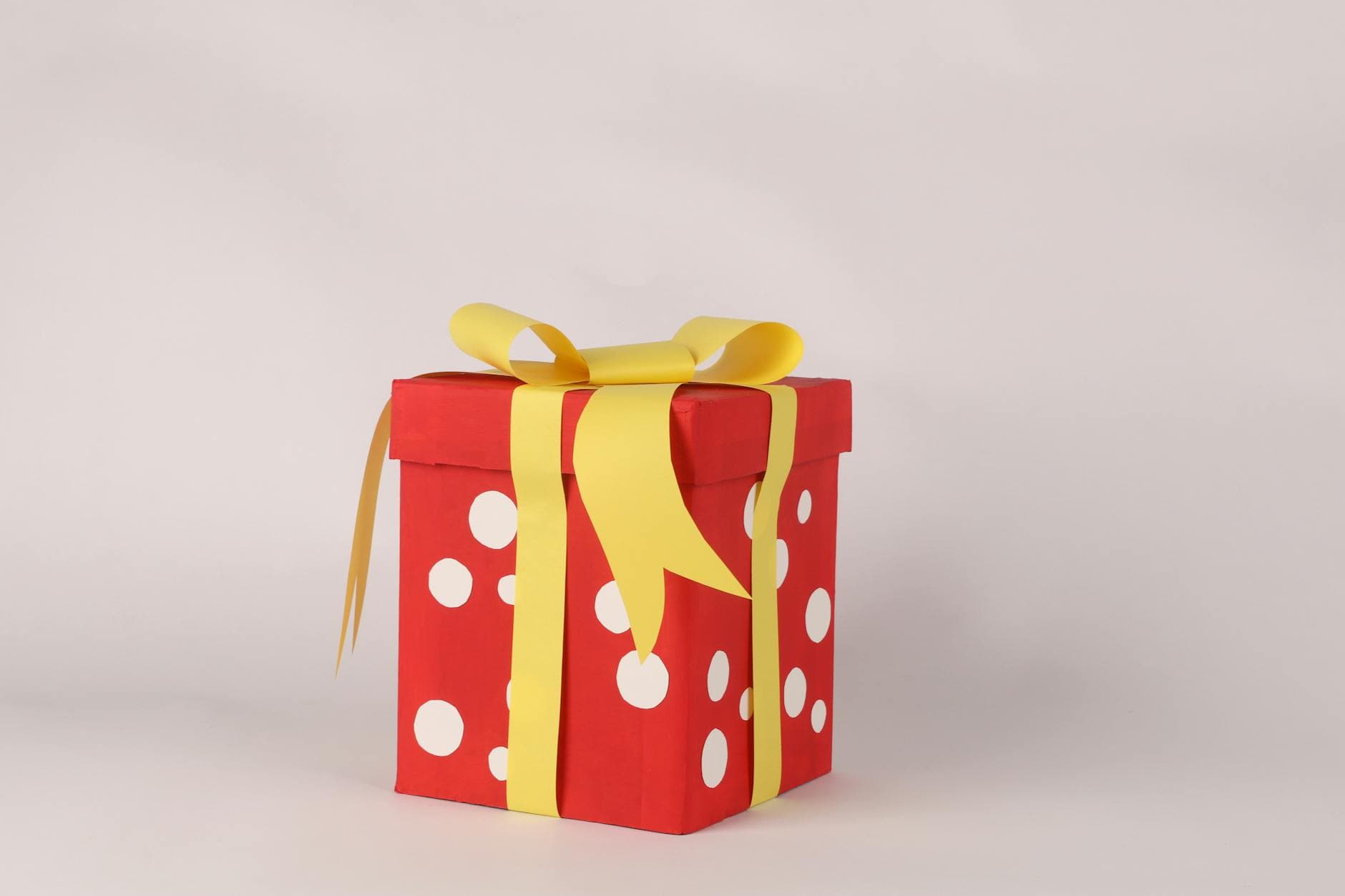 A red gift box with white polka dots and a yellow ribbon, perfect for celebrations.