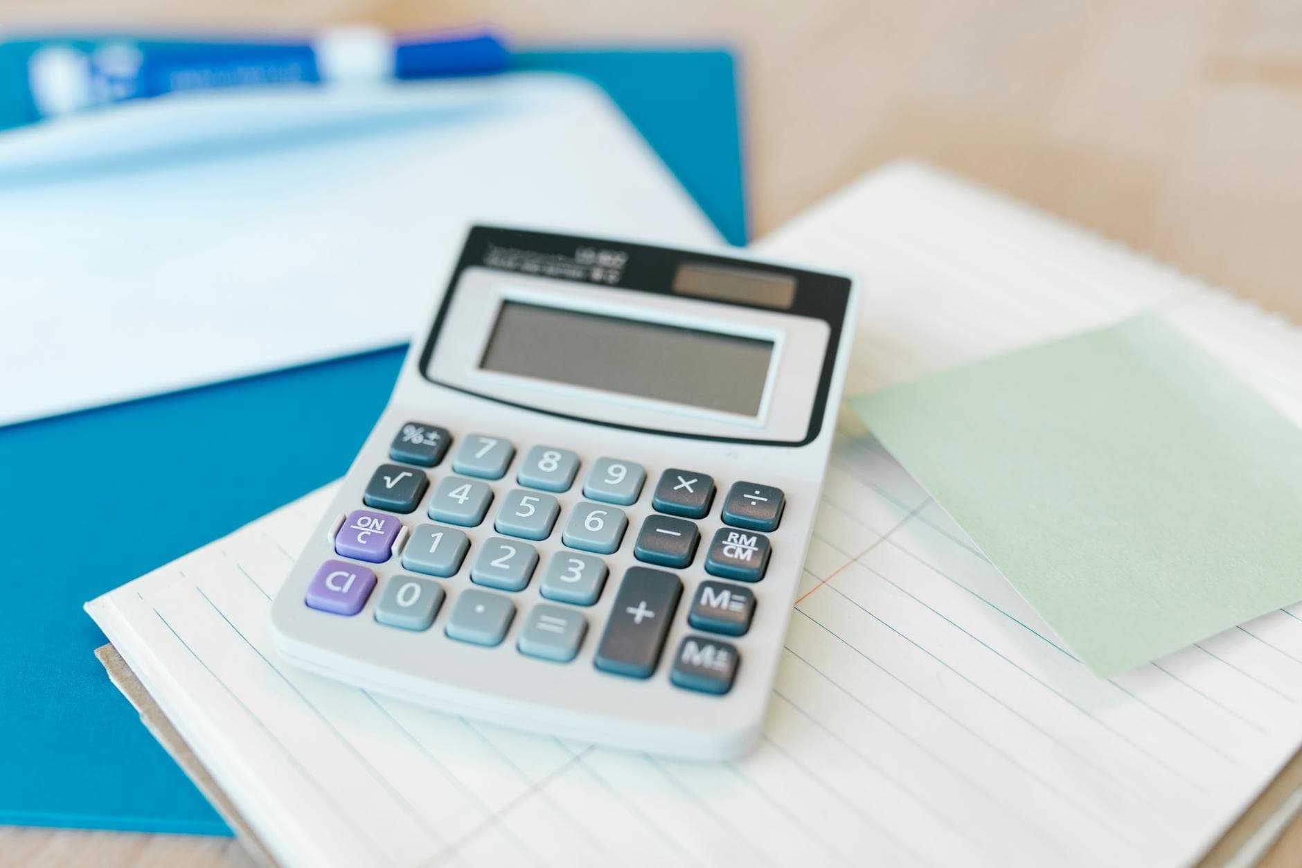 A white calculator on a stack of lined paper with a blue folder, capturing an office setting.