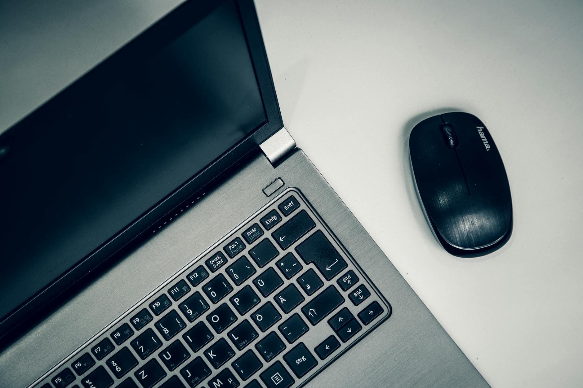 Close-up of a silver laptop and black wireless mouse on a white desk.